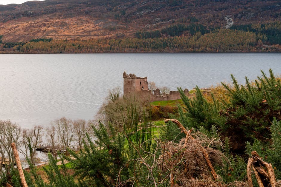 Breathtaking view of Urquhart Castle by Loch Ness surrounded by lush greenery and autumn colors