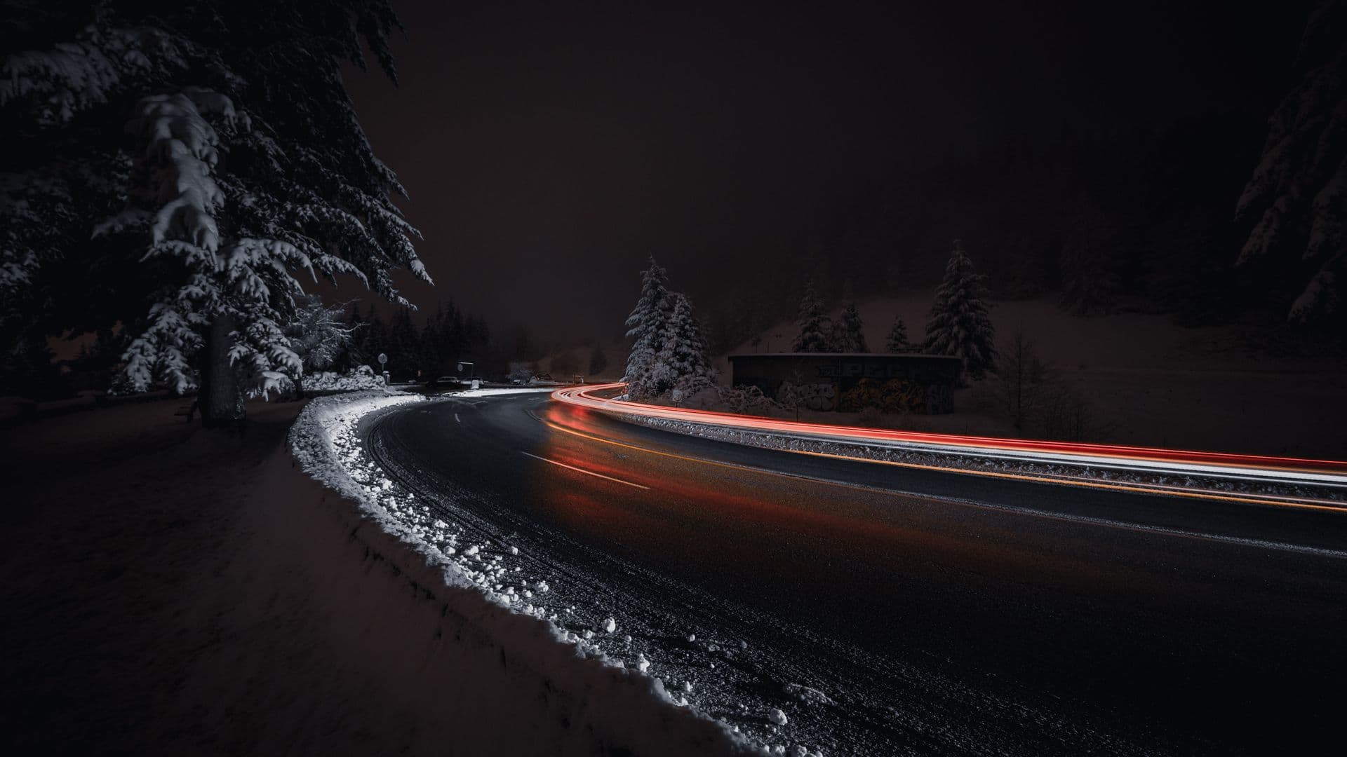 A snow-covered forest road climbing into dark pines at dusk